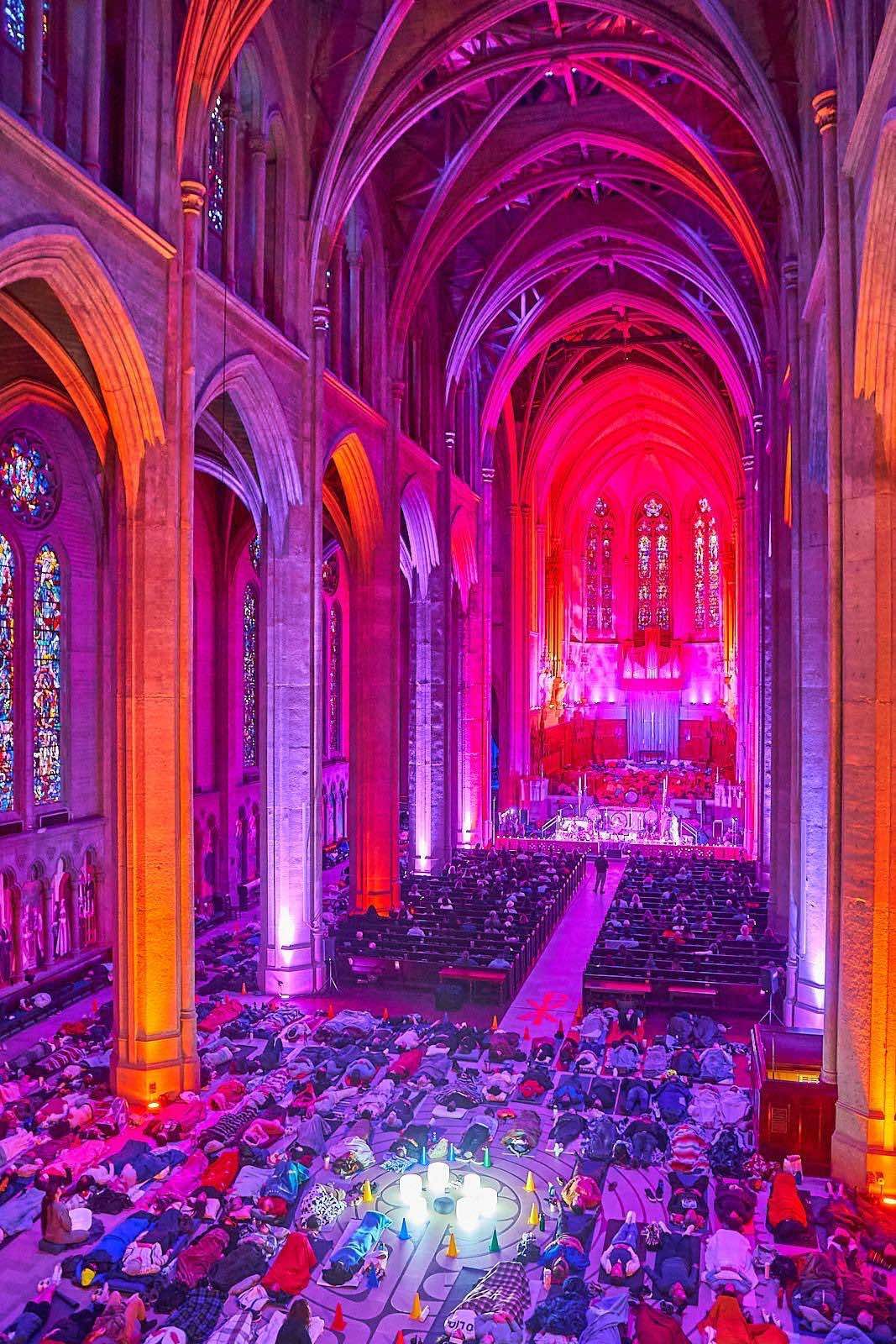 Grace Cathedral glowing pink and gold, its nave filled with people lying down for the Symphony